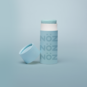 Noz' blue nose sunscreen with the cap open and leaning up against the side of the cylinder sunscreen container, with a light blue background.