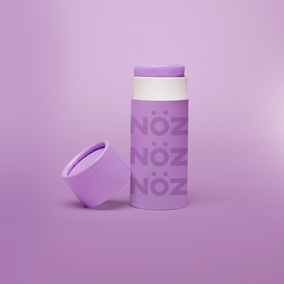 Noz' purple nose sunscreen with the cap open and leaning up against the side of the cylinder sunscreen container, with a light purple background.