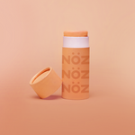 Load image into Gallery viewer, Noz&#39; orange nose sunscreen with the cap open and leaning up against the side of the cylinder sunscreen container, with a light orange background.
