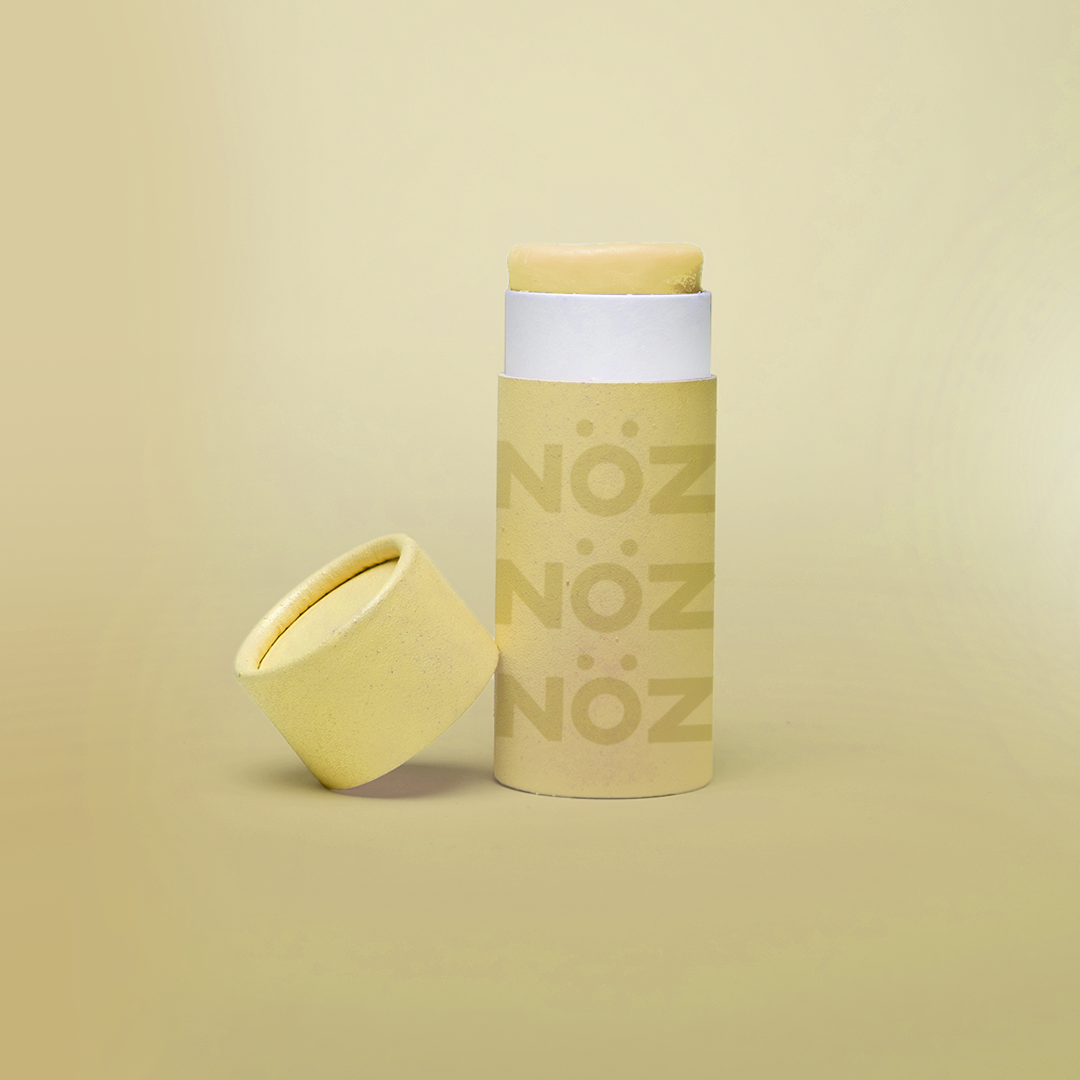 Noz' yellow nose sunscreen with the cap open and leaning up against the side of the cylinder sunscreen container, with a light yellow background.