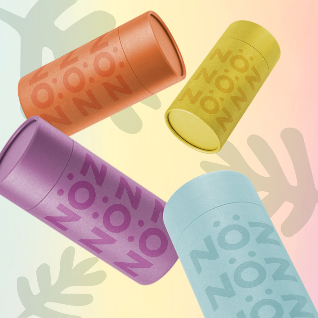 Noz' 4 shades of sunscreen (blue, purple, orange, and yellow) displayed floating in front of a yellow and red gradient background that has three tropical leaves